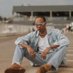 Fashionable young adult wearing denim jacket and jeans sitting outside in urban setting, Brazil.